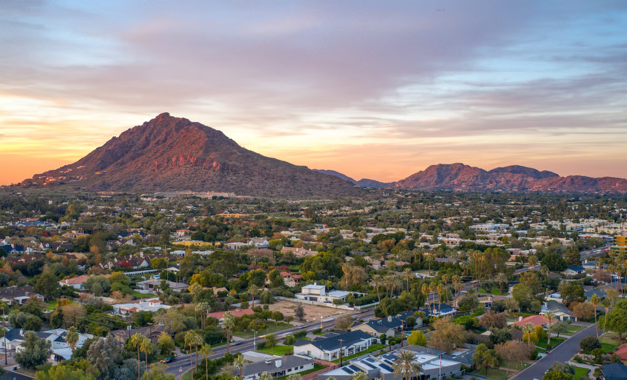 Aerial sunset view over North Phoenix neighborhoods with Camelback Mountain and desert peaks in the distance