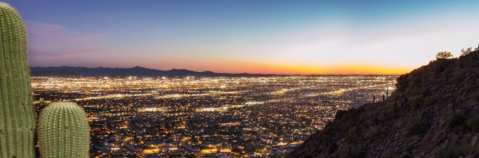 Twilight panoramic view of the greater Phoenix valley from a desert mountain overlook with saguaro cactus in the foreground